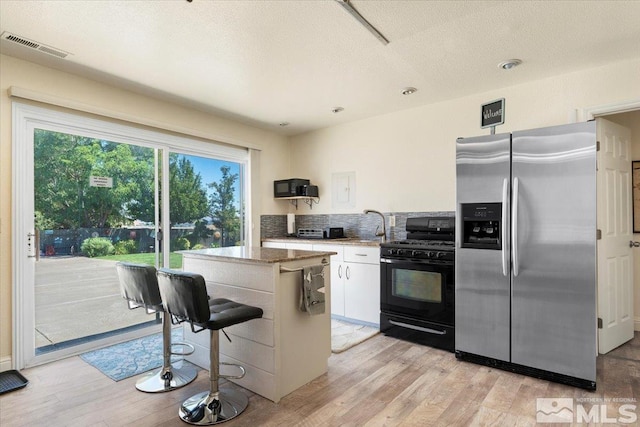 kitchen featuring visible vents, white cabinetry, light wood-style floors, gas stove, and stainless steel fridge