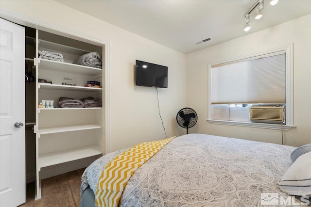 bedroom with cooling unit, wood finished floors, visible vents, and rail lighting