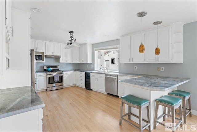 kitchen with under cabinet range hood, a peninsula, light wood-style floors, white cabinets, and appliances with stainless steel finishes