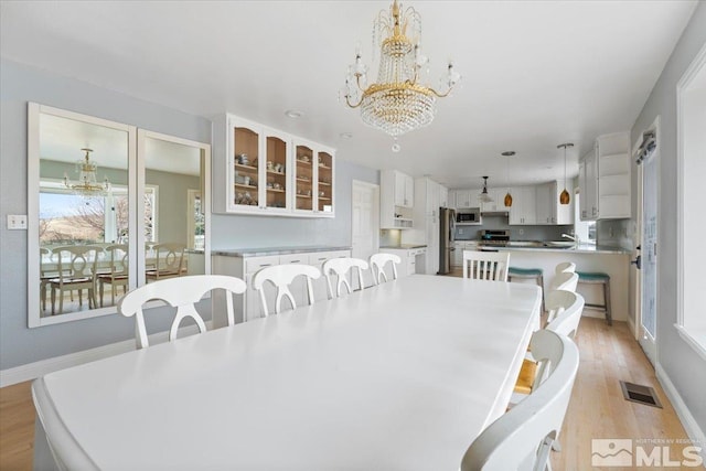 dining room with a chandelier, light wood finished floors, visible vents, and baseboards