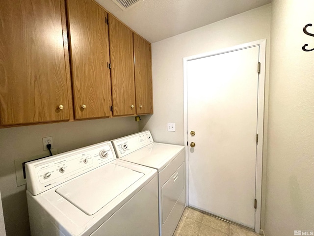 clothes washing area with light tile patterned flooring, washing machine and clothes dryer, and cabinets