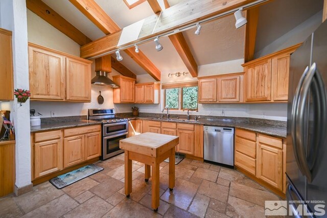 kitchen with vaulted ceiling with beams, appliances with stainless steel finishes, wall chimney exhaust hood, and track lighting