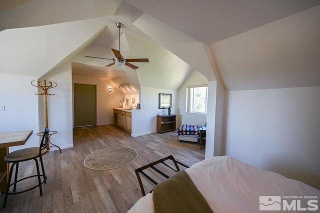 bedroom featuring ceiling fan, hardwood / wood-style floors, vaulted ceiling, ensuite bath, and sink