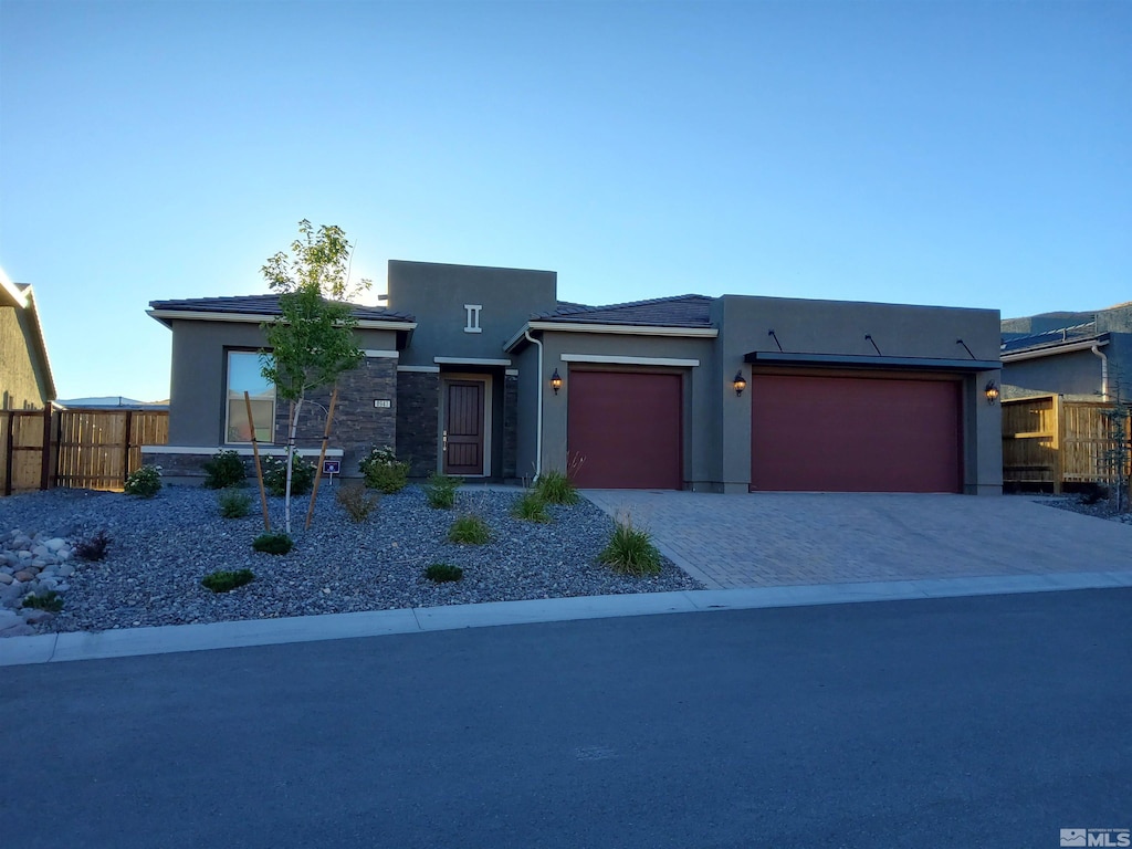 view of front of house with decorative driveway, stucco siding, an attached garage, fence, and stone siding