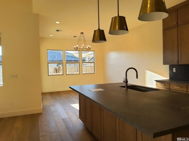 kitchen featuring sink, an inviting chandelier, dark hardwood / wood-style flooring, an island with sink, and decorative light fixtures