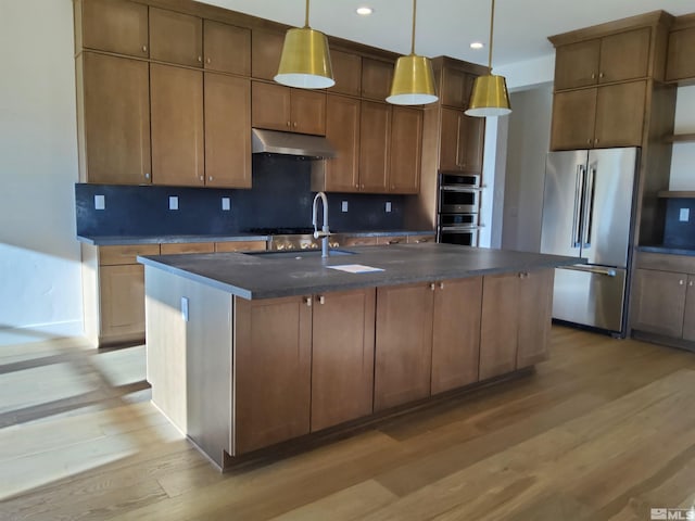 kitchen featuring decorative light fixtures, stainless steel appliances, a center island with sink, and light hardwood / wood-style floors