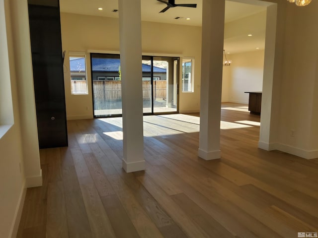 empty room with a wealth of natural light, light hardwood / wood-style flooring, and ceiling fan with notable chandelier