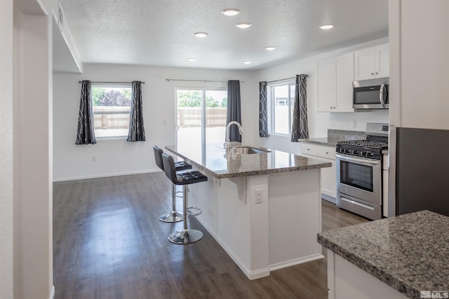 kitchen with sink, a textured ceiling, a kitchen island with sink, white cabinets, and appliances with stainless steel finishes