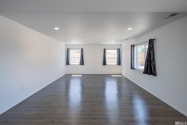 spare room with a textured ceiling, a healthy amount of sunlight, and dark hardwood / wood-style floors