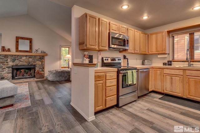 kitchen featuring sink, a stone fireplace, hardwood / wood-style flooring, vaulted ceiling, and stainless steel appliances