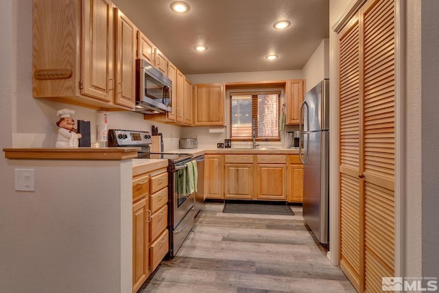 kitchen featuring light brown cabinetry, light hardwood / wood-style flooring, and appliances with stainless steel finishes