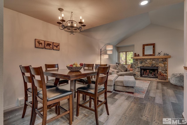 dining space with a notable chandelier, lofted ceiling, hardwood / wood-style floors, and a stone fireplace