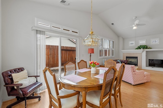 dining area featuring lofted ceiling, light wood-type flooring, a glass covered fireplace, and visible vents