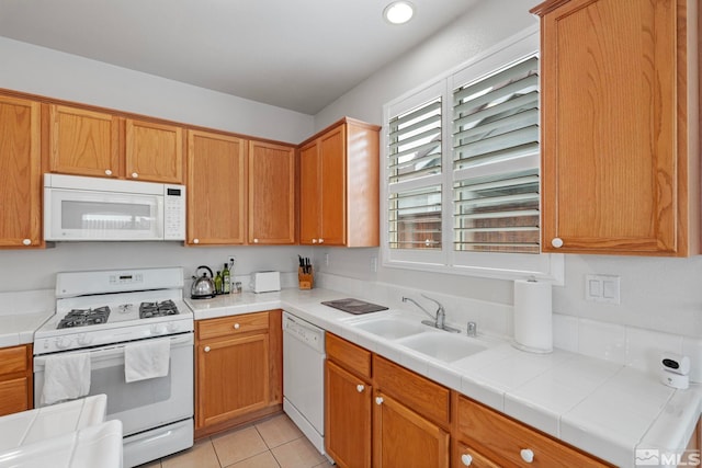 kitchen featuring white appliances, light tile patterned floors, tile countertops, brown cabinets, and a sink