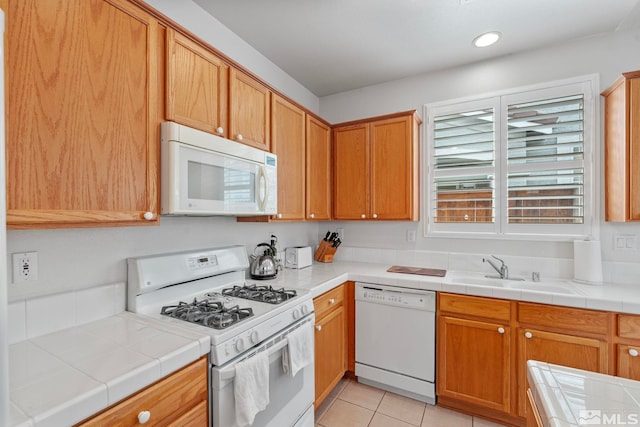 kitchen featuring white appliances, light tile patterned floors, tile counters, a sink, and recessed lighting