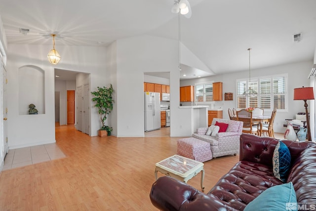 living room with light wood finished floors, visible vents, and high vaulted ceiling