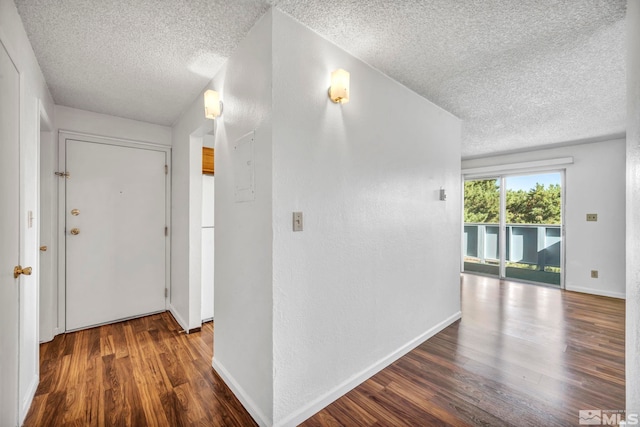 hall featuring a textured ceiling, dark wood-style flooring, and baseboards