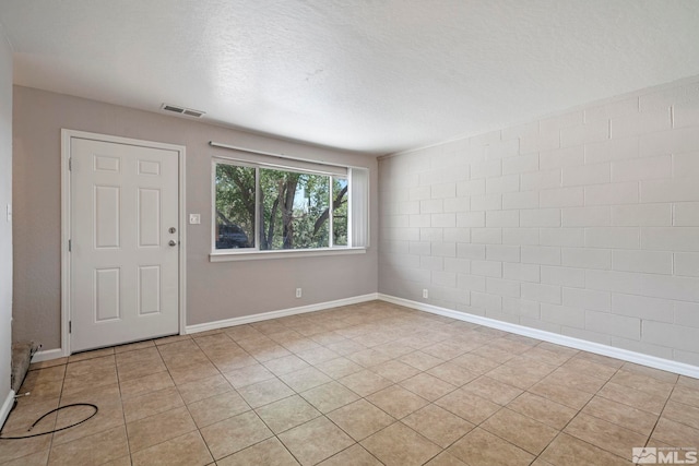 spare room with a textured ceiling, light tile patterned flooring, visible vents, and baseboards