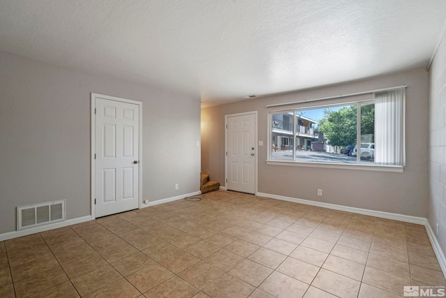 empty room with stairs, a textured ceiling, visible vents, and baseboards