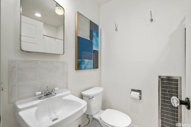 bathroom with toilet, heating unit, tasteful backsplash, and a sink