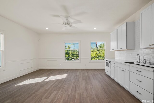 kitchen with white cabinetry, hardwood / wood-style flooring, tasteful backsplash, and stainless steel microwave