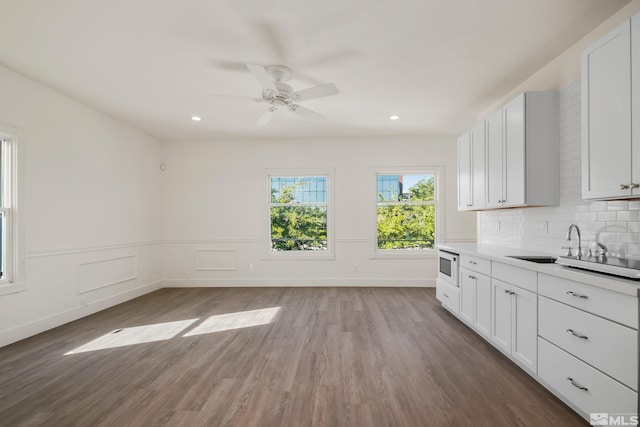 kitchen with white microwave, a sink, wood finished floors, white cabinets, and light countertops