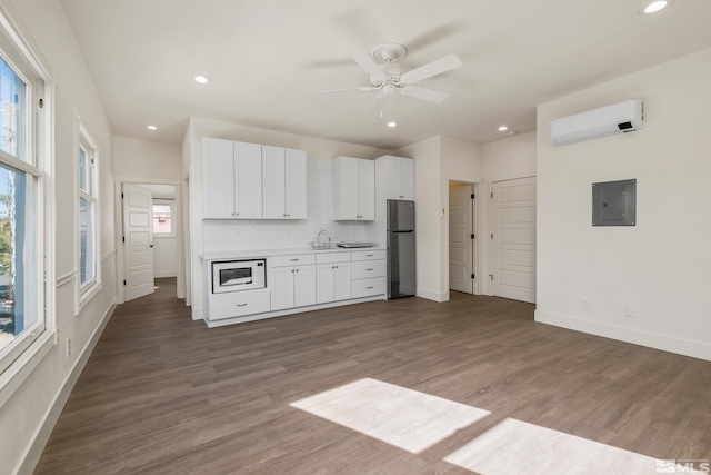 kitchen with electric panel, white microwave, freestanding refrigerator, light countertops, and white cabinetry