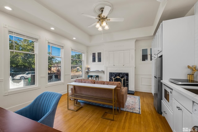 living room with a tray ceiling, a fireplace, recessed lighting, light wood-style floors, and a ceiling fan