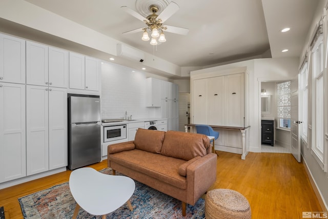 living room featuring sink, ceiling fan, washer / dryer, and light wood-type flooring