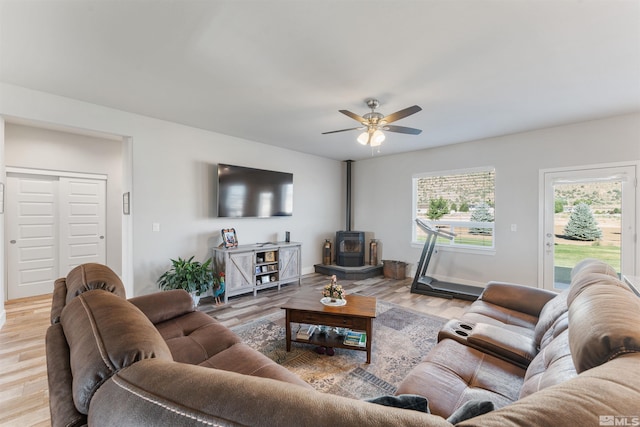 living area featuring a wood stove, light wood-type flooring, and a ceiling fan