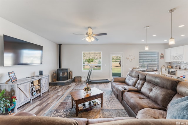 living area with a wood stove, light wood-style flooring, ceiling fan, and recessed lighting