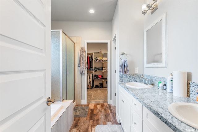 full bath featuring a stall shower, a sink, a spacious closet, and wood finished floors