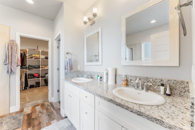 bathroom featuring double vanity, wood finished floors, a sink, and a walk in closet