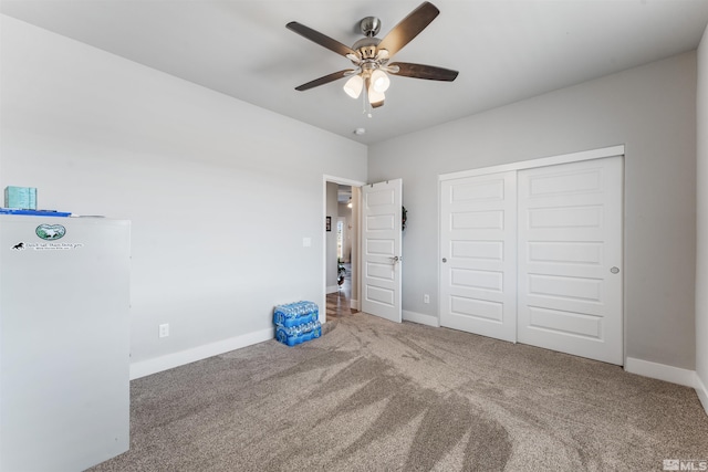 unfurnished bedroom featuring baseboards, a ceiling fan, freestanding refrigerator, carpet floors, and a closet