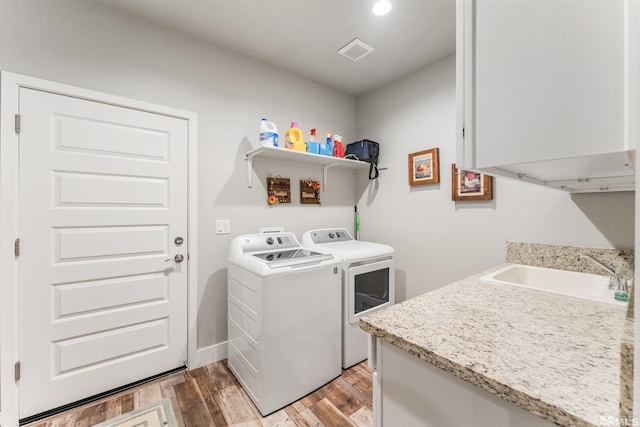 clothes washing area featuring washer and clothes dryer, cabinet space, visible vents, light wood-style flooring, and a sink