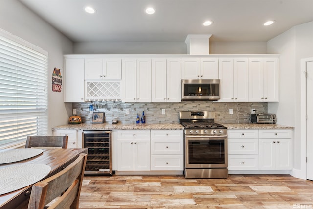 kitchen featuring light wood-type flooring, beverage cooler, white cabinetry, and stainless steel appliances