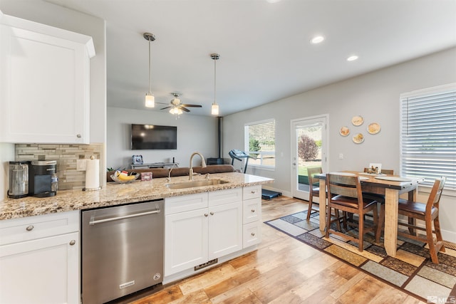 kitchen featuring light wood-style flooring, a peninsula, a sink, stainless steel dishwasher, and backsplash