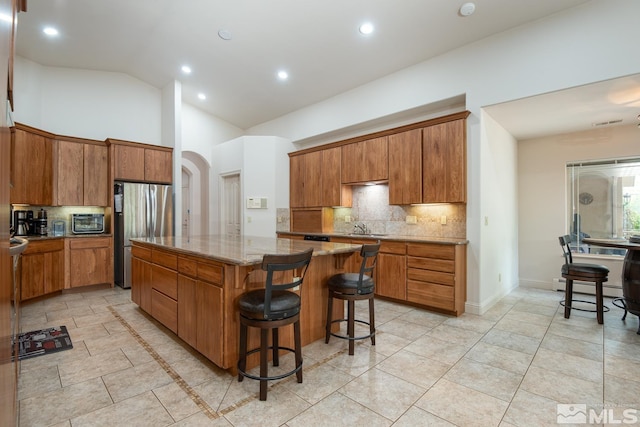 kitchen with arched walkways, brown cabinetry, a kitchen breakfast bar, a center island, and freestanding refrigerator