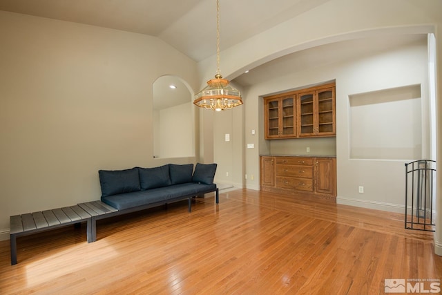 living area featuring light wood finished floors, baseboards, vaulted ceiling, and a notable chandelier