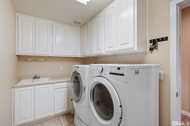 clothes washing area featuring sink, washer and dryer, cabinets, and light tile patterned flooring