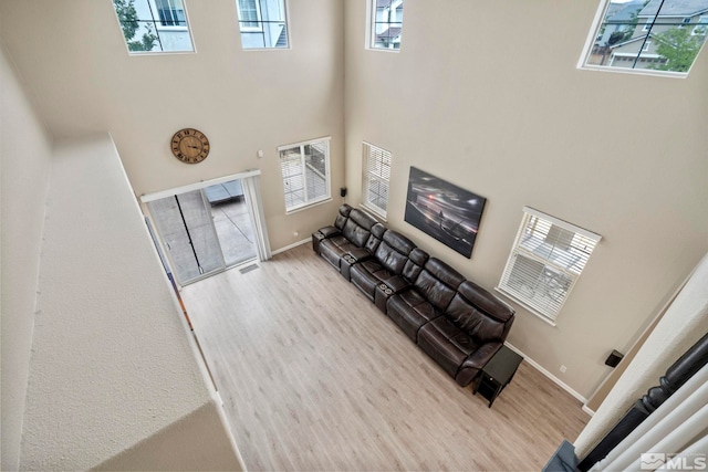 living area with a towering ceiling, visible vents, light wood-style flooring, and baseboards