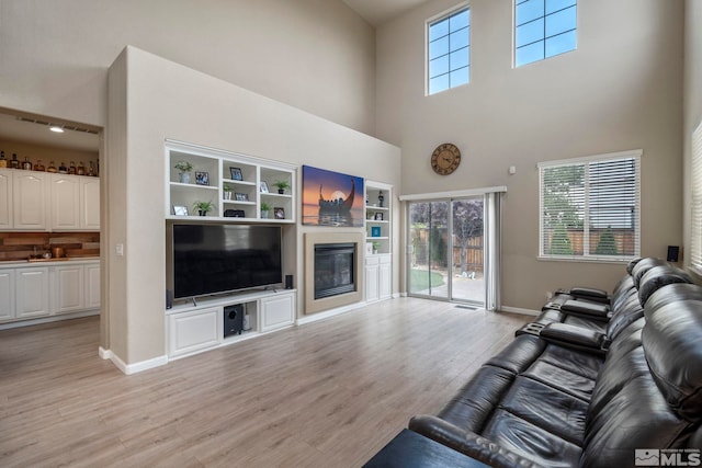 living area featuring light wood-style floors, plenty of natural light, baseboards, and a glass covered fireplace