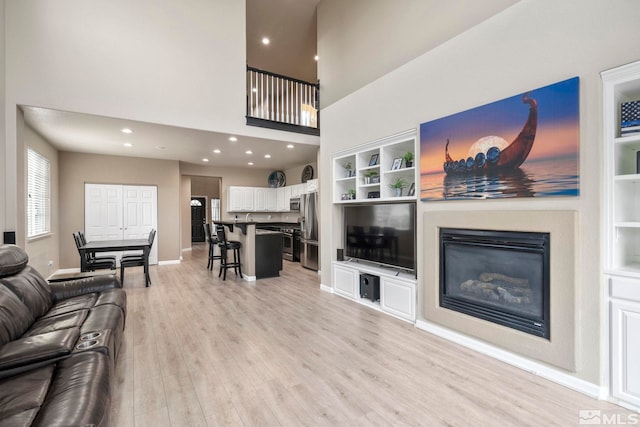 living room featuring built in features, light hardwood / wood-style floors, and a high ceiling