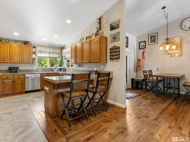 kitchen featuring a breakfast bar, a notable chandelier, light wood-type flooring, stainless steel dishwasher, and lofted ceiling