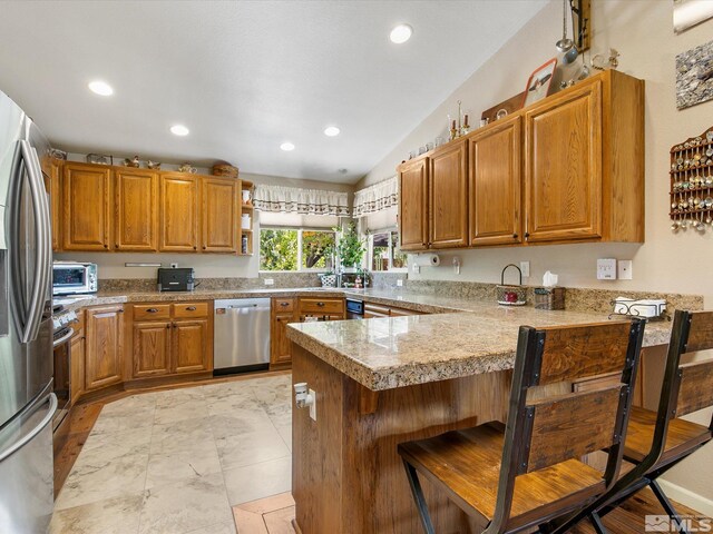 kitchen with a kitchen bar, appliances with stainless steel finishes, light tile patterned floors, kitchen peninsula, and lofted ceiling