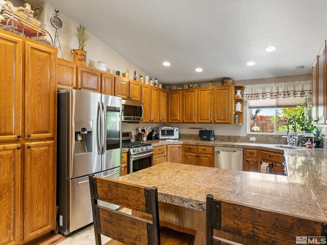 kitchen featuring stainless steel appliances, a kitchen bar, sink, kitchen peninsula, and vaulted ceiling