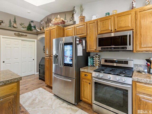 kitchen with appliances with stainless steel finishes, lofted ceiling, and light hardwood / wood-style floors