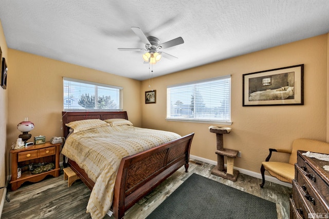 bedroom with a textured ceiling, multiple windows, baseboards, and wood finished floors