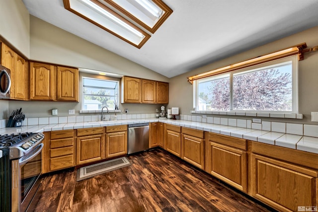 kitchen featuring stainless steel appliances, dark wood-type flooring, tile countertops, and lofted ceiling