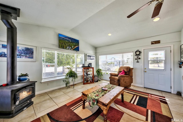 tiled living room featuring ceiling fan, lofted ceiling, and a wood stove